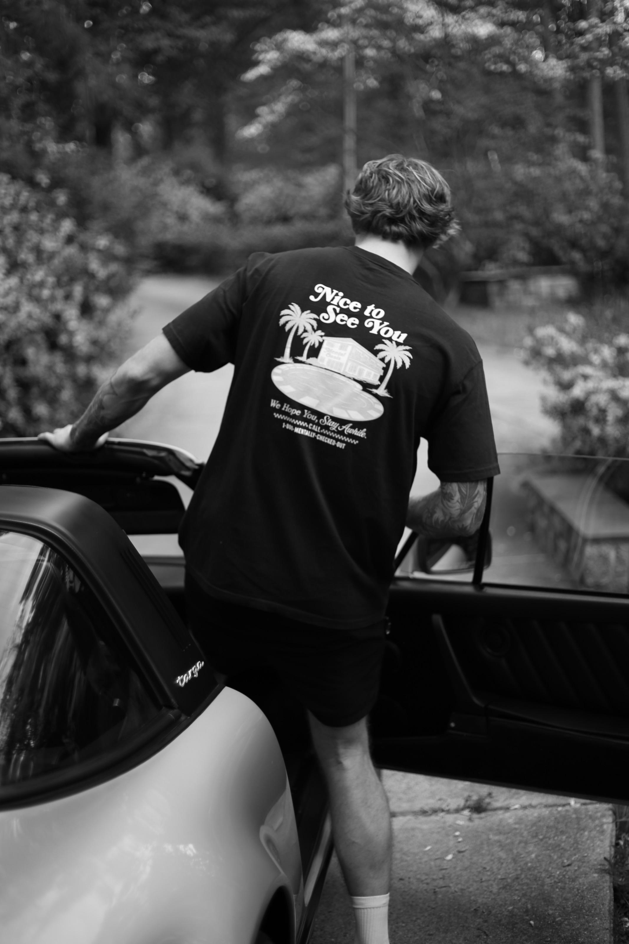 The back of a Nice to See You t-shirt as someone steps into an open Porsche Targa.