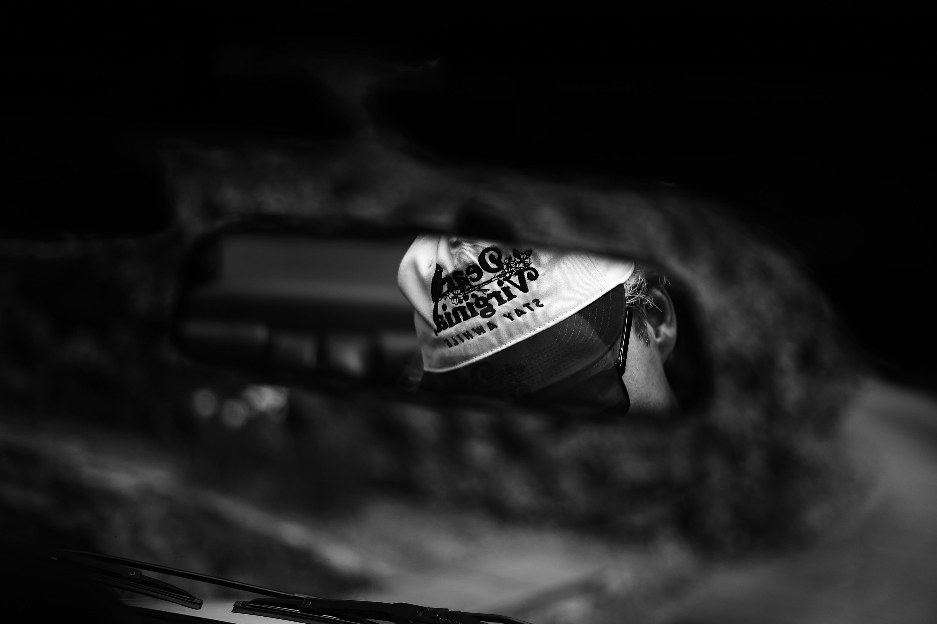 A Dear Virginia cap reflected in a car's rearview mirror, the rest of the frame almost entirely in shadow.